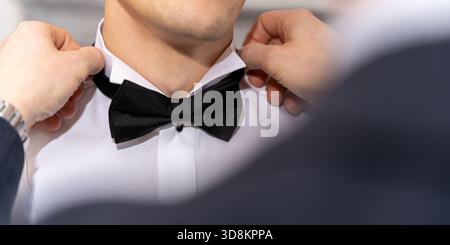Meilleur homme ajustant Groom Black Bow Tie sur chemise blanche pendant la préparation élégante de mariage Banque D'Images