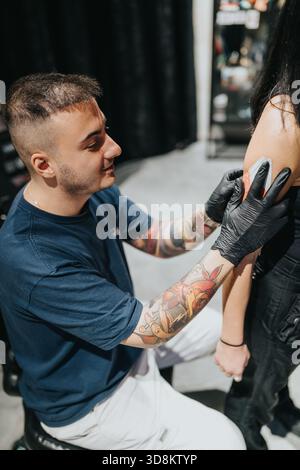 Tatoueur portant des gants encres un tatouage d'épaule sur le client dans un cadre de studio Banque D'Images