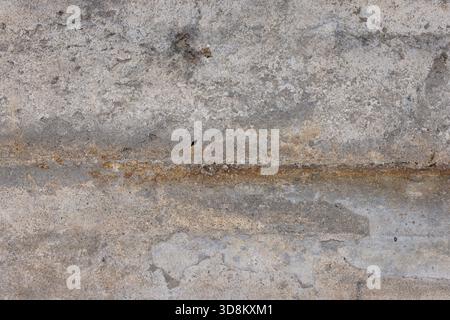Texture de béton rugueuse affichée sur un mur extérieur vieilli. La lumière du jour met en valeur la surface altérée, mettant en valeur son caractère et ses détails uniques. Banque D'Images