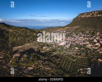 À l'aube, un drone révèle Valldemossa nichée entre des champs en terrasses et des collines rocheuses, ses bâtiments en pierre brillent doucement dans la lumière du matin. Banque D'Images
