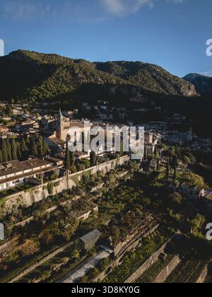 À l'aube, un drone révèle Valldemossa nichée entre des champs en terrasses et des collines rocheuses, ses bâtiments en pierre brillent doucement dans la lumière du matin. Banque D'Images