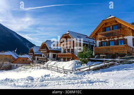 Chalets alpins enneigés sous un soleil d'hiver éclatant avec des montagnes en arrière-plan Banque D'Images