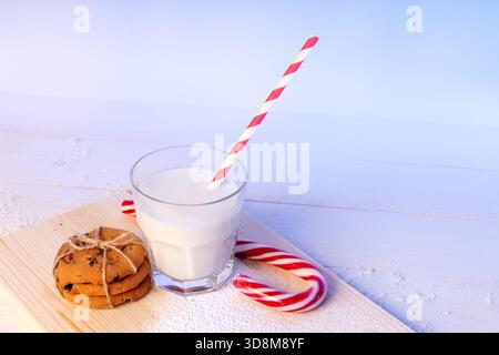 Un verre de lait et une pile de biscuits aux pépites de chocolat sur une planche de bois saupoudrée de sucre en poudre, à côté d'une canne de bonbon rouge et blanche. Simple, fès Banque D'Images