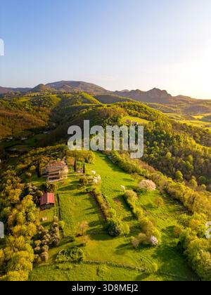 Vue aérienne d'une petite ferme à flanc de colline sur une colline près de la montagne Monte Venda dans les collines Colli Euganei avec le soleil couchant projetant une lumière chaude sur la colline près des rangées de vignes Banque D'Images