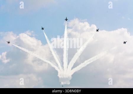 Six avions de chasse exécutent un motif de fumée aérienne parfaitement synchronisé formant une forme fleurie contre un ciel bleu clair, mettant en valeur... Banque D'Images