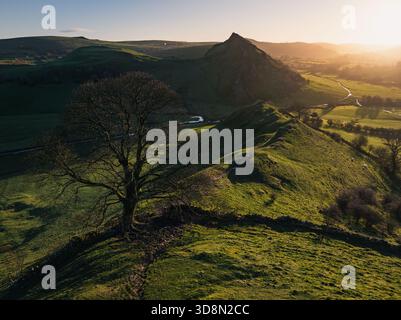Vue aérienne d'un arbre solitaire dresse la garde sur les collines verdoyantes ondulantes, avec le pic accidenté de Chrome Hill silhouette contre le coucher de soleil doré Banque D'Images