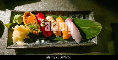 Plateau de sushi assorti avec fruits de mer frais, garnitures et couleurs vives, magnifiquement disposés sur une surface texturée sombre pour un attrait visuel. Banque D'Images