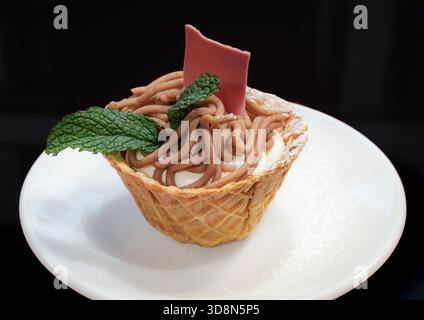 Dessert aux vermicelles suisses avec purée de châtaignes sucrées et crème, garni de menthe et d'une feuille de chocolat rose dans une tasse à gaufres, Zurich, Suisse Banque D'Images