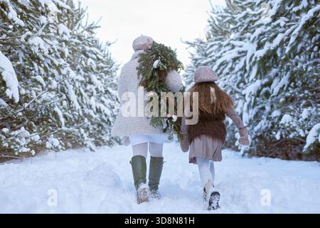 Mère et fille portent une couronne de Noël et marchent à travers une forêt enneigée en hiver, Banque D'Images