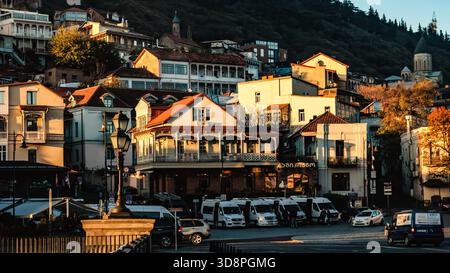 Charmante vue matinale sur le vieux Tbilissi à la lumière du lever du soleil, avec balcons traditionnels en bois, maisons confortables, minibus, et une église nichée au pied de Banque D'Images