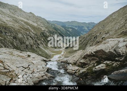Une petite cascade alpine descendant une pente rocheuse avec vue sur la vallée de Wildgerlostal dans les Alpes autrichiennes, entourée par la forêt et mountai Banque D'Images