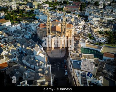 Vue aérienne de l'importante église des Saints Cosmas et Damiano debout haut au milieu d'une mer de maisons de trulli uniques au toit blanc, Alberobello, Pouilles, Banque D'Images