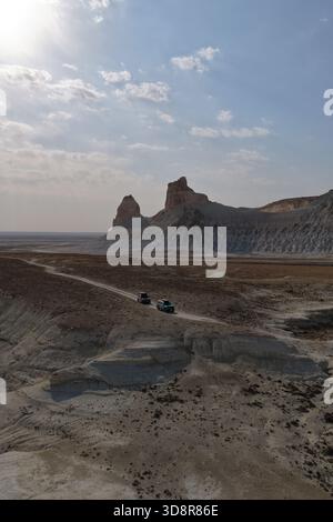 Deux véhicules tout-terrain naviguant sur une piste sinueuse de terre à travers le spectaculaire paysage désertique du canyon de Bozjyra, avec des falaises escarpées et des formations rocheuses uniques Banque D'Images