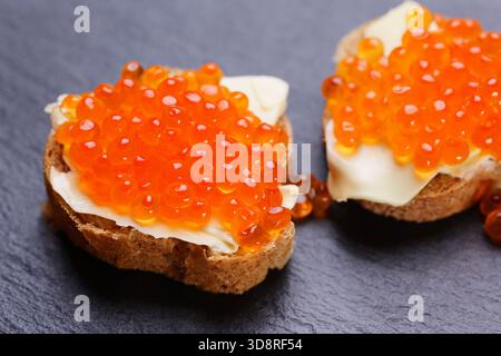 Sandwichs au caviar rouge sur plaque de pierre d'ardoise noire. Un délicieux apéritif de caviar de truite sur une tranche de pain avec du fromage à la crème. Œufs de saumon. Banque D'Images