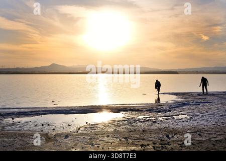 Deux hommes silhouettes au lac salé de Larnaca, à Chypre, l'un marchant dans l'eau et l'autre debout sur le rivage pendant un coucher de soleil lumineux l'après-midi Banque D'Images