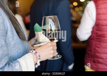 Femme aime le vin lors d'un événement tout en étant entourée d'invités indistincts. Banque D'Images