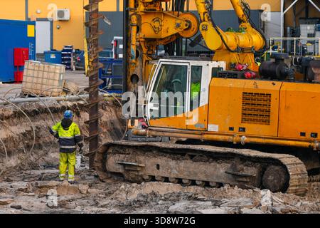 Machine de forage lourde fonctionnant sur le chantier de construction avec un ouvrier supervisant l'excavation des fondations Banque D'Images