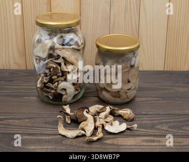 Champignons porcini séchés et champignons marinés dans des bocaux avec des tranches en vrac sur une table rustique en bois Banque D'Images