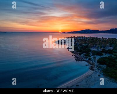 Vue aérienne d'une côte tranquille au coucher du soleil, avec un ciel orange chaud reflétant sur l'eau bleue.Sardaigne, Italie Banque D'Images