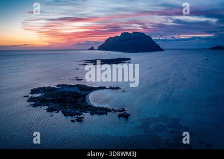 Une scène côtière tranquille au crépuscule comprend une île lointaine, une mer bleue et un ciel pastel, Sardaigne, Italie Banque D'Images