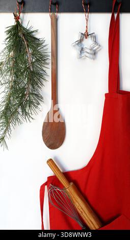 Un tablier de cuisine rouge avec un petit rouleau à pâtisserie en bois et un fouet dans la poche. Confectionner des gâteaux et des biscuits de Noël. Noël et période des fêtes. Banque D'Images