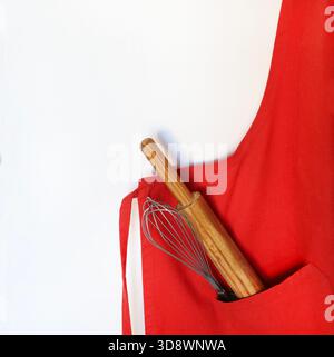 Un tablier de cuisine rouge avec un petit rouleau à pâtisserie en bois et un fouet dans la poche. Confectionner des gâteaux et des biscuits de Noël. Noël et période des fêtes. Banque D'Images