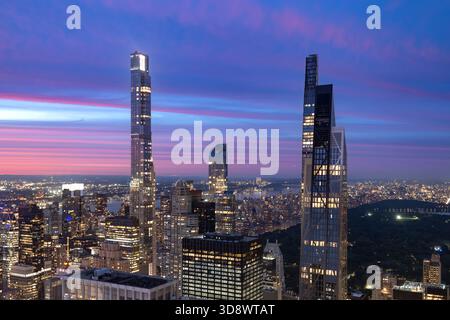 La verticalité spectaculaire des tours du New York City Billionaires Row s'illumine contre un ciel nocturne vibrant, avec l'étalement urbain qui s'étend en dessous. Banque D'Images