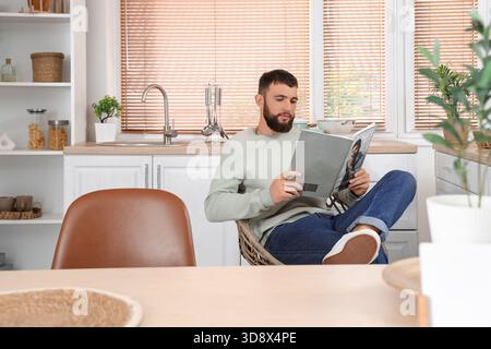 Jeune homme barbu lisant le magazine dans la cuisine Banque D'Images