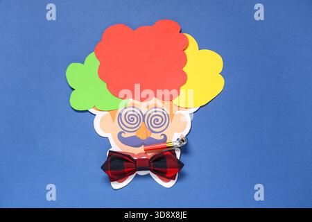 Visage de clown en papier avec noeud papillon et sifflet de fête sur fond bleu Banque D'Images