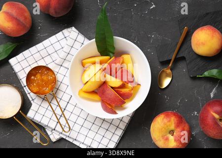 Pêches tranchées dans un bol, mesurer des tasses de sucre et de confiture sur fond grunge gris Banque D'Images