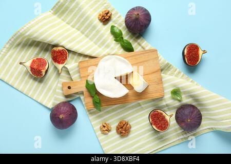 Planche avec du fromage camembert savoureux, des figues fraîches mûres et des feuilles de basilic sur fond bleu Banque D'Images