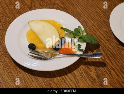 Assiette blanche avec des tranches de divers fruits colorés décorés de feuilles de menthe ; désert, collation saine, dessert végétarien. Banque D'Images
