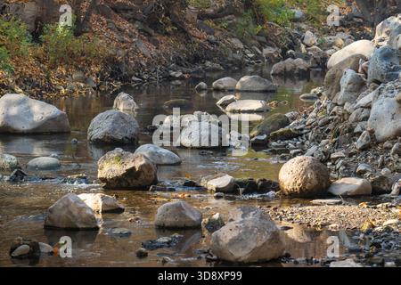 Une rivière avec une rive rocheuse et quelques gros rochers dans l'eau. Les rochers sont dispersés dans toute la rivière, avec certains plus près de la rive et d'autres f Banque D'Images