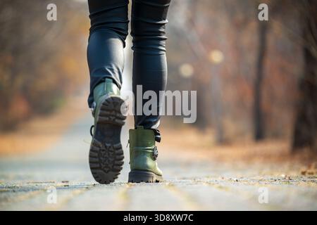 Une personne marche sur un chemin dans les bois portant des bottes vertes. Les bottes sont imperméables et ont une couleur verte. La personne porte un pantalon noir et Banque D'Images