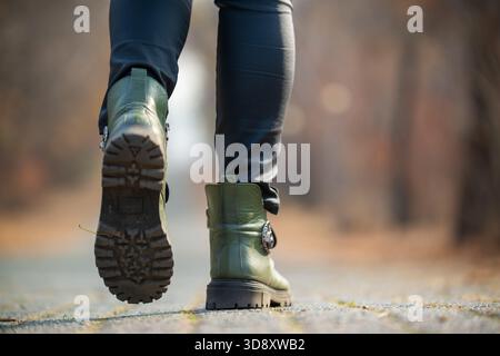 Une personne portant des bottes vertes et un pantalon noir marche sur une route. Les bottes sont en cuir et ont un aspect brillant. Les jambes de la personne sont vi Banque D'Images