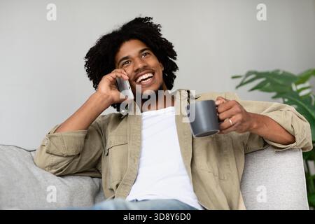 Heureux homme afro-américain aime le café et parle au téléphone tout en se relaxant à la maison Banque D'Images