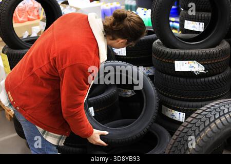 Homme choisissant un pneu de voiture dans un magasin d'automobiles, inspectant les roues en caoutchouc parmi les piles de pneus neufs. Photo de haute qualité Banque D'Images