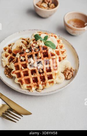 Gaufres maison avec garniture de miel, noix et banane sur l'assiette avec couverts dorés, vue de dessus Banque D'Images