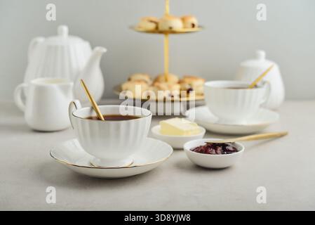 Thé anglais dans d'élégantes tasses en porcelaine blanche servi avec des scones, du lait, du beurre et de la confiture, thé Five O'Clock Banque D'Images