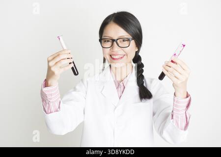 Jeune scientifique asiatique vérifiant le sang dans un tube Banque D'Images