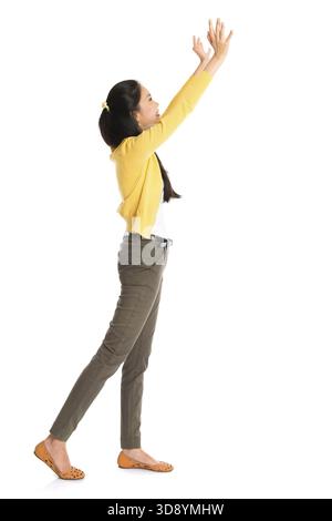 Vue latérale ou profil d'une fille asiatique bras vers le haut comme pousser quelque chose loin, pleine longueur debout isolé sur fond blanc Banque D'Images