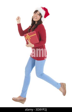 Femme Noël en marche et holding gift wearing Santa hat. Debout dans un corps entier isolé sur fond blanc. Smiling woman portrait d'une belle Banque D'Images