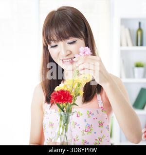 Heureuse femme au foyer asiatique avec tablier arrangeant des fleurs à vase. Jeune femme à l'intérieur vivant le mode de vie à la maison Banque D'Images