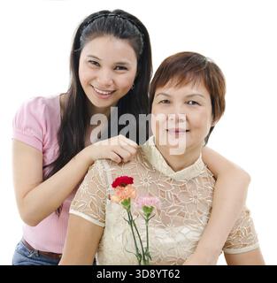 Mère âgée tenant la fleur d'oeillet, fille adulte embrasse maman, isolée sur fond blanc. Portrait de famille asiatique mixte Banque D'Images