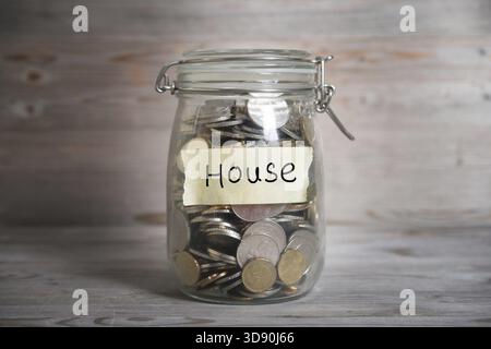 Pièces de monnaie dans un pot en verre avec étiquette de maison, concept financier. Fond en bois vintage avec lumière dramatique Banque D'Images