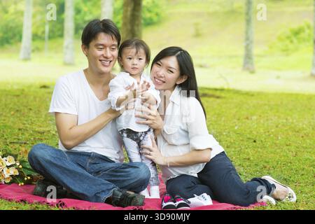 Joyeuse activité de plein air en famille asiatique. Parents et fille ayant, pique-niquer sur la pelouse verte du jardin Banque D'Images