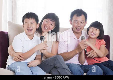 Famille à la maison. Portrait of a happy Asian family singing karaoke par microphone dans le salon Banque D'Images