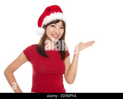 Femme de Noël asiatique présentant / montrant l'espace de copie debout dans le chapeau de Père Noël. Isolé sur fond blanc souriant regardant la caméra Banque D'Images
