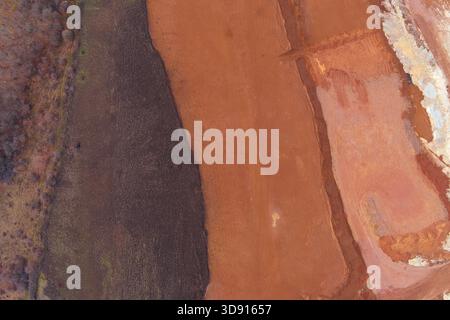 Prise de vue par drone capturant la forte frontière organique entre un sol sombre et flou et un champ de labourage chaud et brun rougeâtre. Le contraste net crée une texture d'arrière-plan abstraite dynamique. Banque D'Images