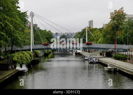 Un pont suspendu piétonnier orné de jardinières enjambe un canal bordé d'arbres avec des bateaux amarrés le long des rives par une journée couverte à Helsinki, en Finlande. Banque D'Images